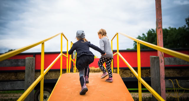 Two children running up an orange ramp with yellow railings, with a red and black structure in the background.