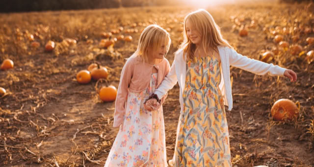 Two children walking through a pumpkin patch at sunset.