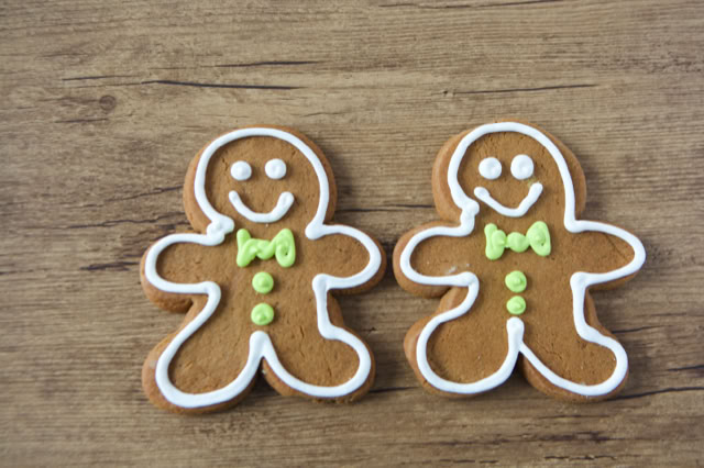 Two gingerbread cookies with white icing outlines, green bow ties, and buttons, placed on a wooden surface.