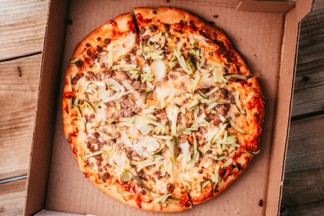 A pizza with various toppings in an open cardboard box on a wooden surface.