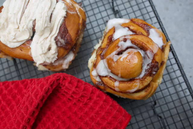 Two cinnamon rolls with icing on a cooling rack, next to a red cloth.